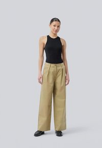 Tan wide-leg trousers with pleats, paired with a black sleeveless top. The outfit features smooth fabric and a relaxed silhouette, worn with black shoes.