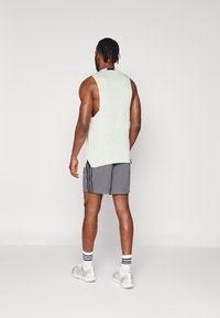 Light green sleeveless tank top with a rounded hem and side slits, paired with gray shorts featuring black vertical stripes.