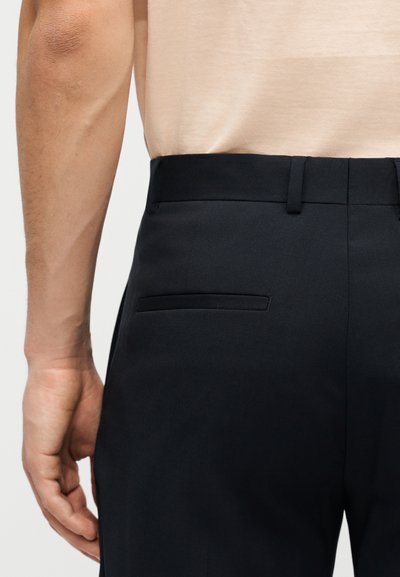 Κοντινή λήψη ενός ατόμου που φοράει μαύρο παντελόνι με πίσω τσέπη welt και μπεζ πουκάμισο κρυμμένο μέσα.