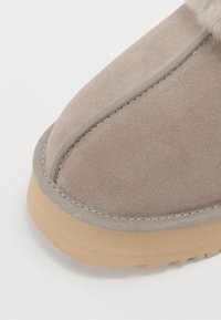 Chaussure en daim beige avec une semelle épaisse de couleur marron clair, une couture détaillée et une garniture en tissu doux autour de la zone des orteils.