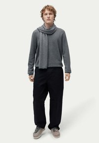 Grå ulltröja med draperad halsringning, kombinerad med lösa svarta byxor och ljusgrå skor. Enkel, ren design med neutrala färger.