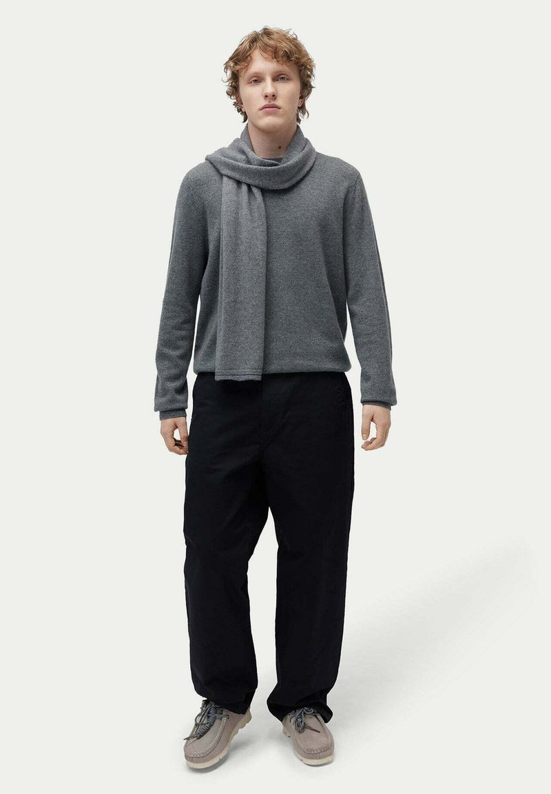 Grå ulltröja med draperad halsringning, kombinerad med lösa svarta byxor och ljusgrå skor. Enkel, ren design med neutrala färger.