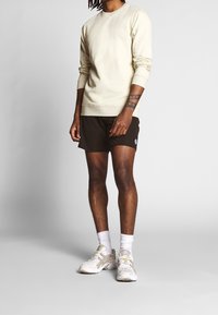 Jasnobeżowa bluza z długimi rękawami w zestawieniu z ciemnobrązowymi szortami. Dopełnieniem stroju są białe i szare sneakersy z subtelnymi akcentami.