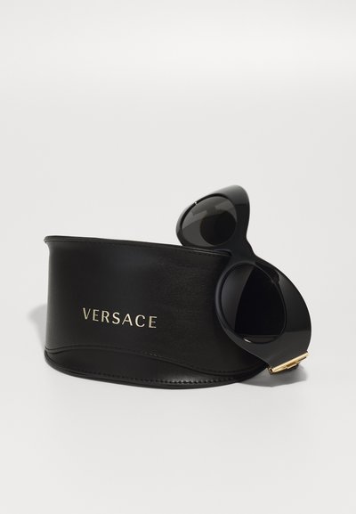 Lunettes de soleil noires avec une finition brillante, accompagnées d'un étui en cuir noir arborant un logo doré "VERSACE" et un design courbé.