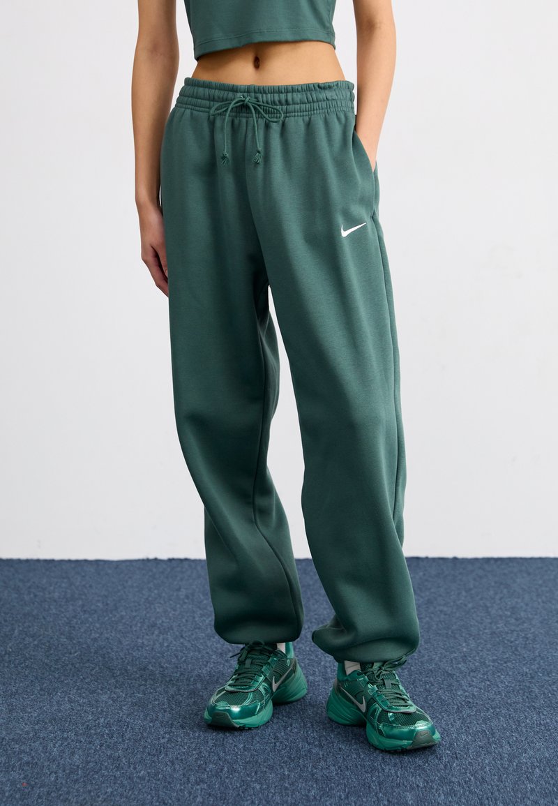 Roheline, mugavuslõikega dressipüksid elastse vöökoha ja paelaga, millel on vasakul reiel väike valge Nike logo.