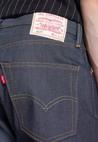 Mörkblå denimjeans med en röd Levi's-tagg, kontrasterande gula sömmar och den klassiska bågformen på bakfickorna.