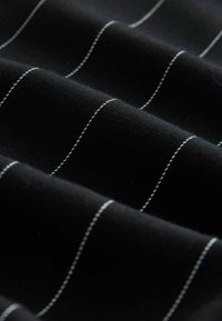 Tessuto nero con righe bianche, caratterizzato da una texture liscia e un leggero lucido. Le righe corrono orizzontalmente lungo la lunghezza del materiale.