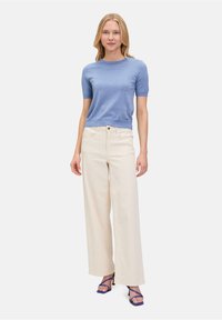 Maglietta a maniche corte di colore azzurro chiaro abbinata a pantaloni a gamba larga crema a vita alta e tacchi blu con cinturini. Tessuto semplice e strutturato.