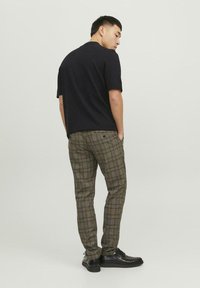 Sort, kortærmet skjorte parret med grønne og brune ternede bukser og sorte sko, der viser en afslappet pasform og klassiske mønstre.