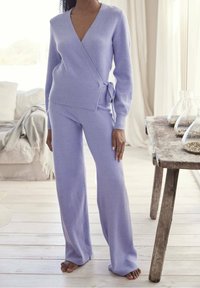 Lichtpaarse gebreide wikkeltrui met strikdetail en lange mouwen, gecombineerd met bijpassende brede broek, beide gemaakt van zachte, gestructureerde stof.