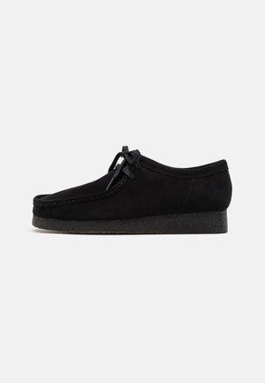 Zwarte suède schoenen met een rond teenontwerp, een vetersluiting aan de voorkant en een gestructureerde zwarte rubberen zool. Gladde bovenkant met subtiele stikseldetails.