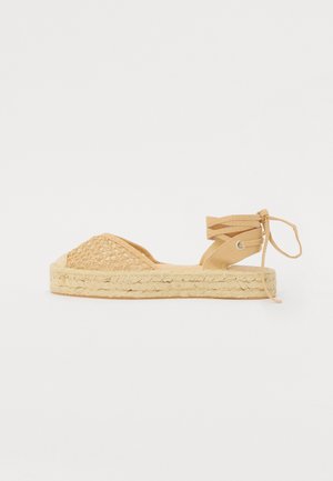 Sandal de espadrilha em tom claro com parte superior trançada, bico redondo e sola de juta. Tira no tornozelo com laços e detalhe em metal.