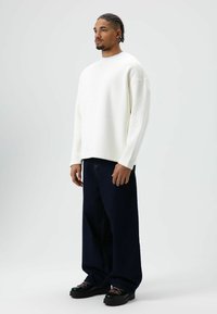 Witte sweatshirt met een ontspannen pasvorm, gecombineerd met oversized donkerblauwe spijkerbroek en zwarte schoenen met roze veters.