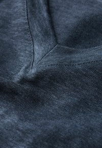 Tmavě modrá texturovaná tkanina s tkaným vzorem, která má diagonální švový detail a jemný, mírně skvrnitý vzhled.