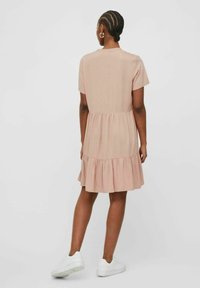 Short-sleeved, knee-length dress in soft pink fabric with a tiered, ruffled skirt and a round neckline, paired with white sneakers.