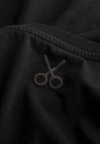 Zwarte stof met een getextureerd, donkergrijs geborduurd schaarlogo. Glad oppervlak met zichtbare stiksels langs de randen.