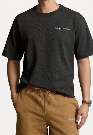 Mand iført sort Polo Ralph Lauren t-shirt og brune snøreshorts med Polo Ralph Lauren-logo på begge.