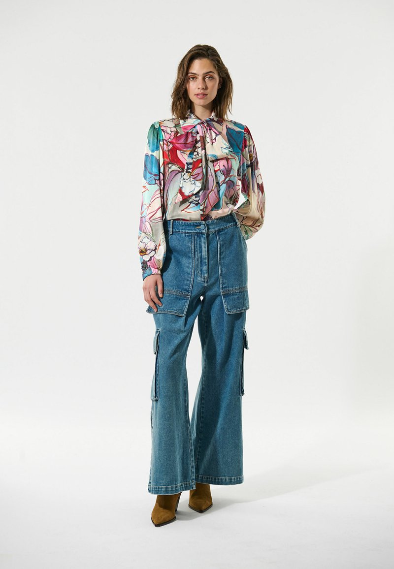 Blusa con estampado floral y lazo en el cuello, combinada con pantalones cargo de mezclilla azul de pierna ancha con bolsillos laterales y botas marrones hasta el tobillo.