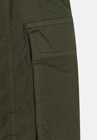 Žalios audinio krovinių kišenės uždarymas su sklende ir matoma dviguba siūlė ant kišenės ir aplink esančios vietos.