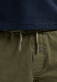 Marineblauw katoenen T-shirt, zoom boven lichte olijfgroene broek van gestructureerde stof. Verstelbaar trekkoord met metalen tips.