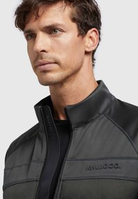 Black and gray zip-up jacket with a high collar, featuring a smooth texture, contrasting seam lines, and a branded accent on the chest.