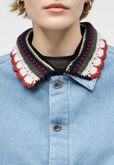 Κοντινό πλάνο ατόμου που φοράει ανοιχτό μπλε τζιν μπουφάν με πολύχρωμο γιακά πλεξίματος και χρυσούς κρίκους στα αυτιά, με τα χείλη ελαφρώς ανοιχτά.