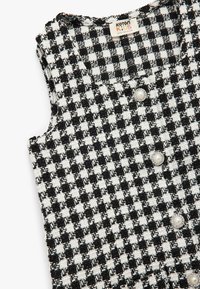 Zwart-wit houndstooth patroon vest van een gestructureerde stof, met ronde parelachtige knopen en een mouwloos ontwerp.