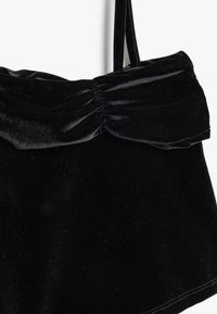Schwarze Samt-Handtasche mit strukturierter Form, die oben mit einer Schleifendetails verziert ist, aus weichem Material gefertigt und mit zwei schlanken Tragegriffen ausgestattet.