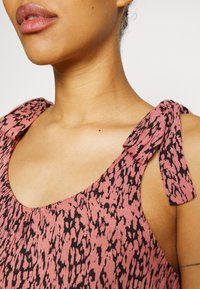 Vestido rosa com padrão abstrato preto, decote largo e laços nos ombros. O tecido parece leve e de textura suave.