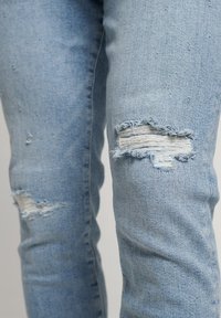 Jeans de mezclilla azul claro desgastados que cuentan con parches de rodilla deshilachados y un diseño ajustado, con una textura suave y un leve desteñido.