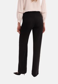 Czarne, skrojone spodnie o prostym kroju. Materiał ma gładką teksturę. U dołu znajduje się subtelne rozcięcie. W zestawieniu z jasną bluzką.