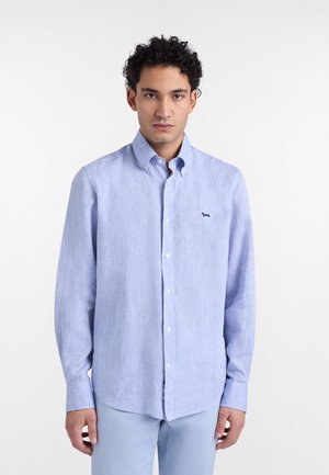 Camisa azul claro con botones, hecha de tela texturizada, con un pequeño logo bordado en el pecho y mangas largas con puños abotonados.