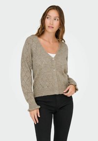 Stickad cardigan i en ljus taupe-färg, med ett diamantmönster, v-ringning och fem knappar framtill. Ribbad nederkant och ärmslut.