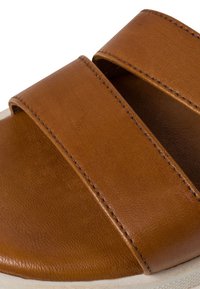 Brown leather slide sandal with two wide straps. Textured surface and visible stitching detail. Rounded edge and white rubber sole.