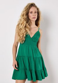 Abito verde con corpino aderente, gonna a strati e spalline sottili regolabili. Tessuto testurizzato con un design smock in vita.