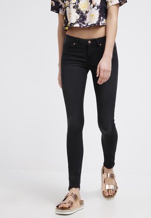 Black skinny jeans with a smooth texture, paired with brown sandals featuring metallic accents. Cropped floral top with purple and yellow hues.