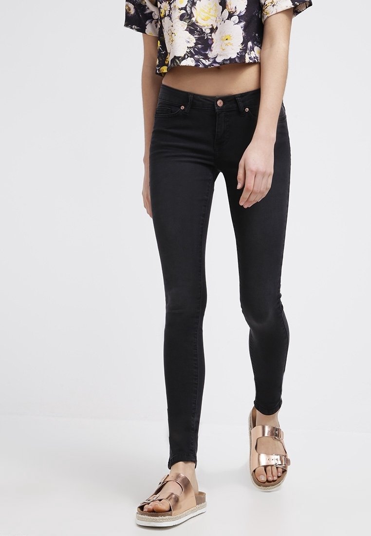 Svart skinny jeans med en mjuk textur, kombinerat med bruna sandaler med metalliska detaljer. Kort blommig topp i lila och gula nyanser.