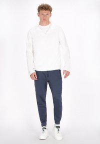 Hvid zip-up sweatshirt med lange ærmer, parret med navy joggerbukser med sidelommer og en tapered pasform. Hvide sneakers fuldender outfittet.