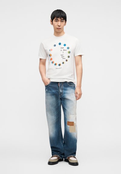 Λευκό γραφικό t-shirt με κυκλικό πολύχρωμο μοτίβο και κείμενο, συνδυασμένο με ανοιχτό μπλε τζιν παντελόνι φαρδύ σε ίσια γραμμή με φθαρμένες λεπτομέρειες και πατς. Καθημερινά παπούτσια.