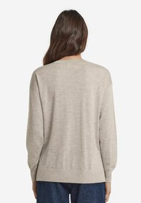 Jasno beżowy sweter o luźnym kroju, z prążkowanym dekoltem i mankietami. Gładka tekstura z minimalną ilością szwów, noszony na ciemnych dżinsowych spodniach.