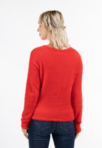 Rode fuzzy trui met lange mouwen, ronde hals en een iets losse pasvorm. Gecombineerd met donkerblauwe skinny jeans. De textuur van de stof is zacht.