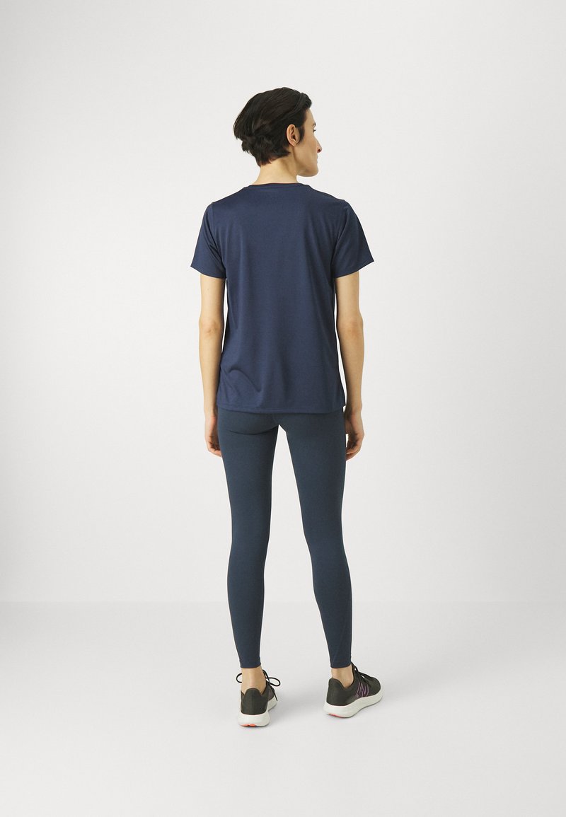 T-shirt de sport à manches courtes bleu marine associé à des leggings foncés et des chaussures de course noires, présenté de dos.