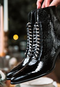 Botine negre din piele ecologică de crocodil cu vârfuri ascuțite și detalii argintii la șireturi. Finisaj cu luciu intens, cusături detaliate.