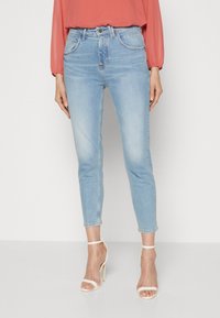 Vaaleansiniset farkut, joissa on keskipituinen vyötärö, kapeneva lahje, haalistuneita yksityiskohtia ja klassinen viiden taskun muotoilu, yhdistettyinä valkoisiin remmikenkiin.