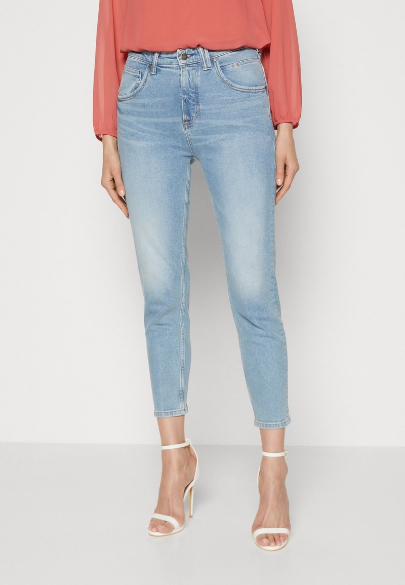 Vaaleansiniset farkut, joissa on keskipituinen vyötärö, kapeneva lahje, haalistuneita yksityiskohtia ja klassinen viiden taskun muotoilu, yhdistettyinä valkoisiin remmikenkiin.