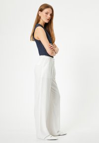Haut sans manches côtelé bleu marine associé à un pantalon large blanc, présentant une texture lisse et une silhouette évasée. Design simple et lignes épurées.