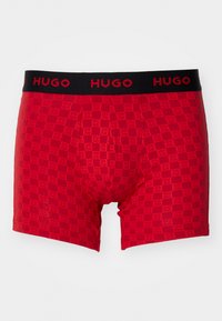 Red boxer briefs with a checkerboard pattern, featuring a black elastic waistband with "HUGO" printed in bold red letters.