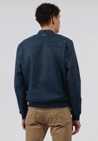 Veste bomber bleu marine avec une texture douce et mate, des poignets et un ourlet côtelés, et une petite étiquette logo au dos du cou.