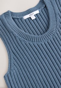 Pull sans manches en maille côtelée bleue avec un col rond et une étiquette blanche portant la mention "NEXT" cousue à l'intérieur du col.