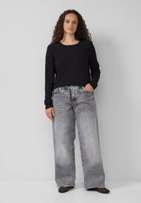 Zwarte geribbelde lange mouw top gecombineerd met vervaagde grijze wijd uitlopende jeans. De outfit wordt aangevuld met zwarte schoenen met een gestifte ontwerpelement.
